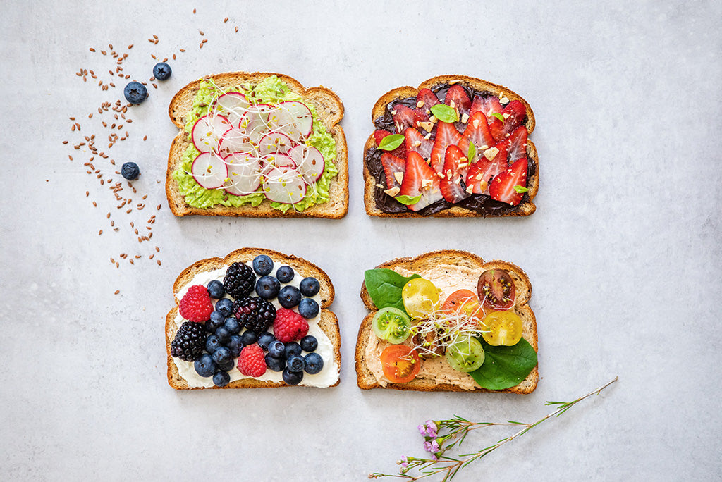 Four pieces of toast topped with various ingredients, including radish, avocado, strawberries, berries, and tomatoes.