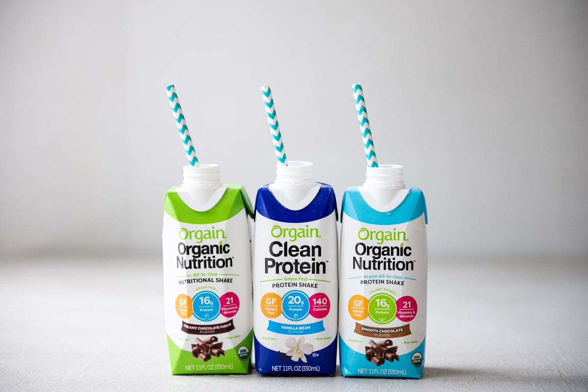 Three cartons of Orgain protein shakes with straws: Vanilla Bean, Clean Protein Vanilla Bean, and Iced Cafe Mocha.