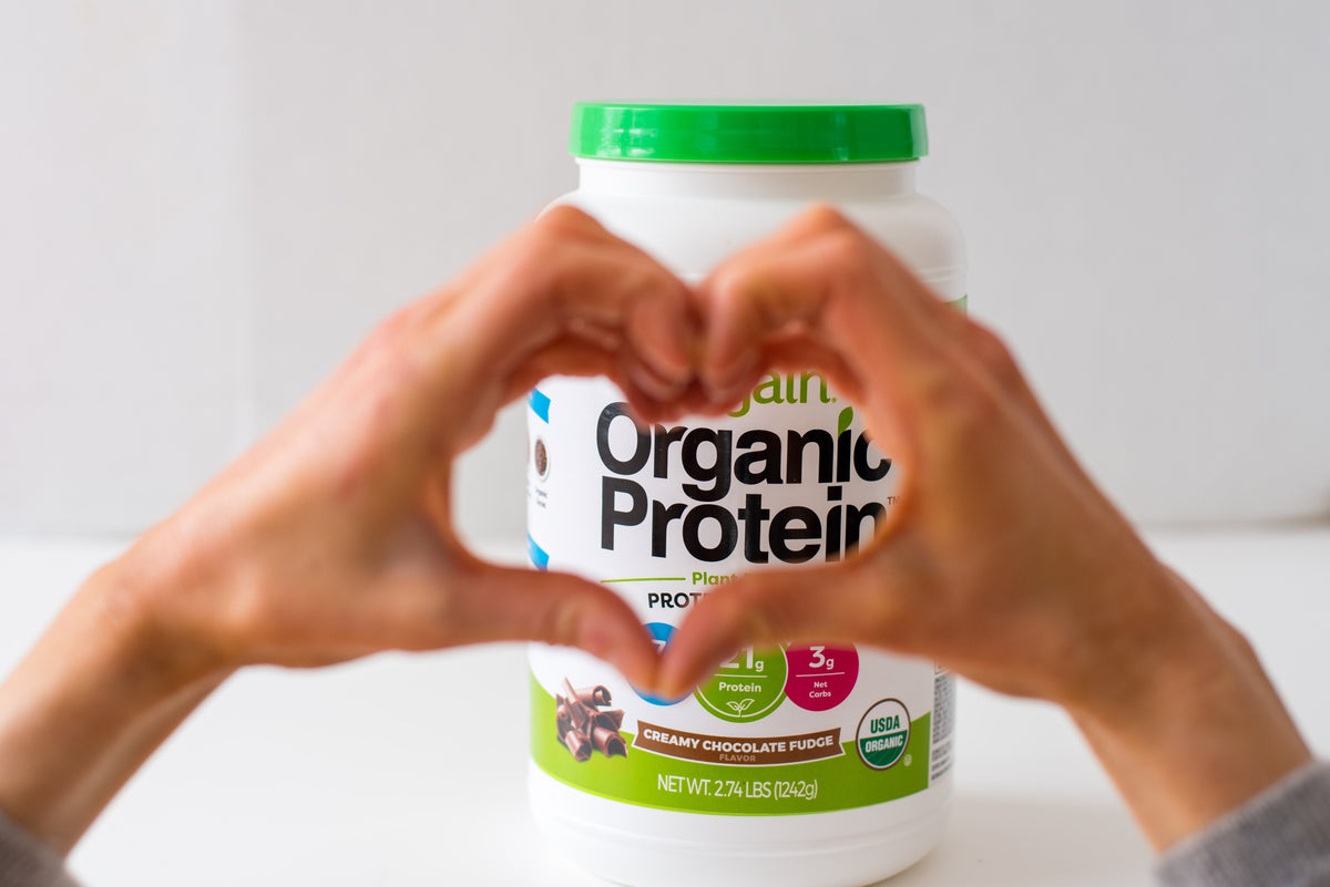 someone holding heart hands over an orgain protein powder canister