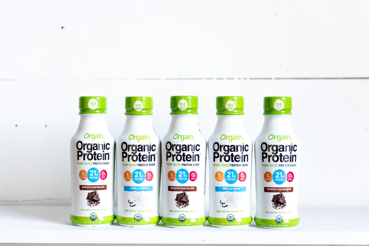 Five bottles of Orgain Organic Protein shakes are lined up against a white backdrop. Three bottles are Vanilla Bean flavor, and two are Creamy Chocolate Fudge flavor. Each bottle highlights 21 grams of protein on a white label with a green cap.