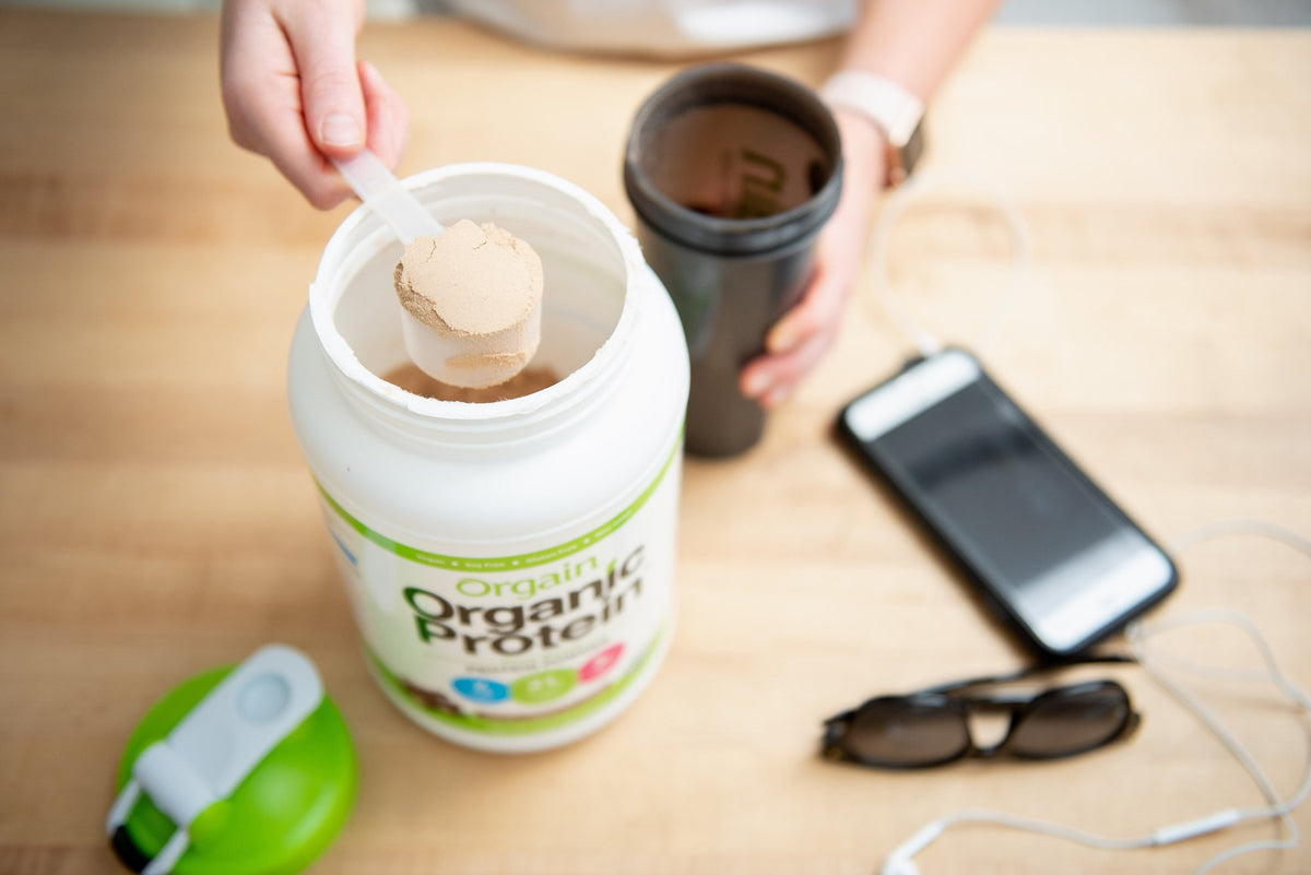 person scooping orgain protein powder into a shaker bottle