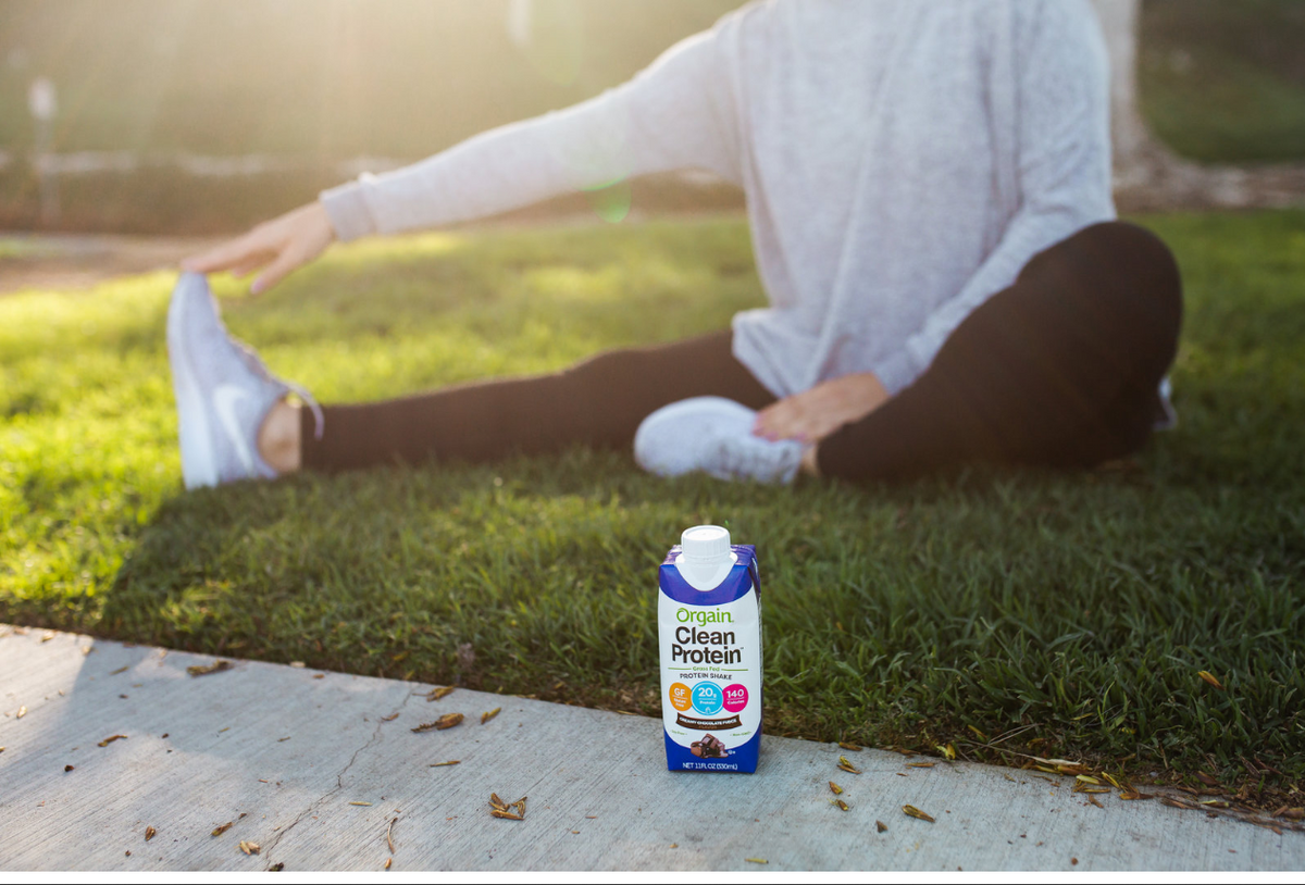 A woman stretching behind a Clean Protein shake from Orgain