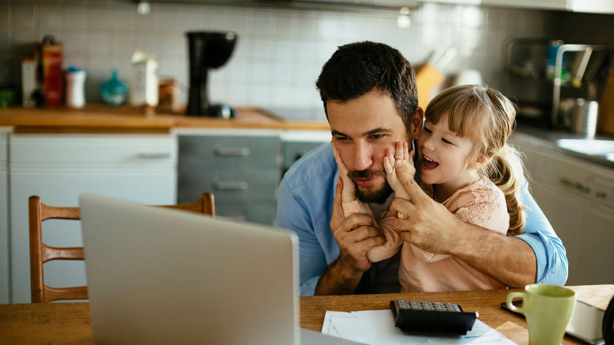 A man and a young girl smile at a laptop with documents and a calculator on a modern kitchen table.