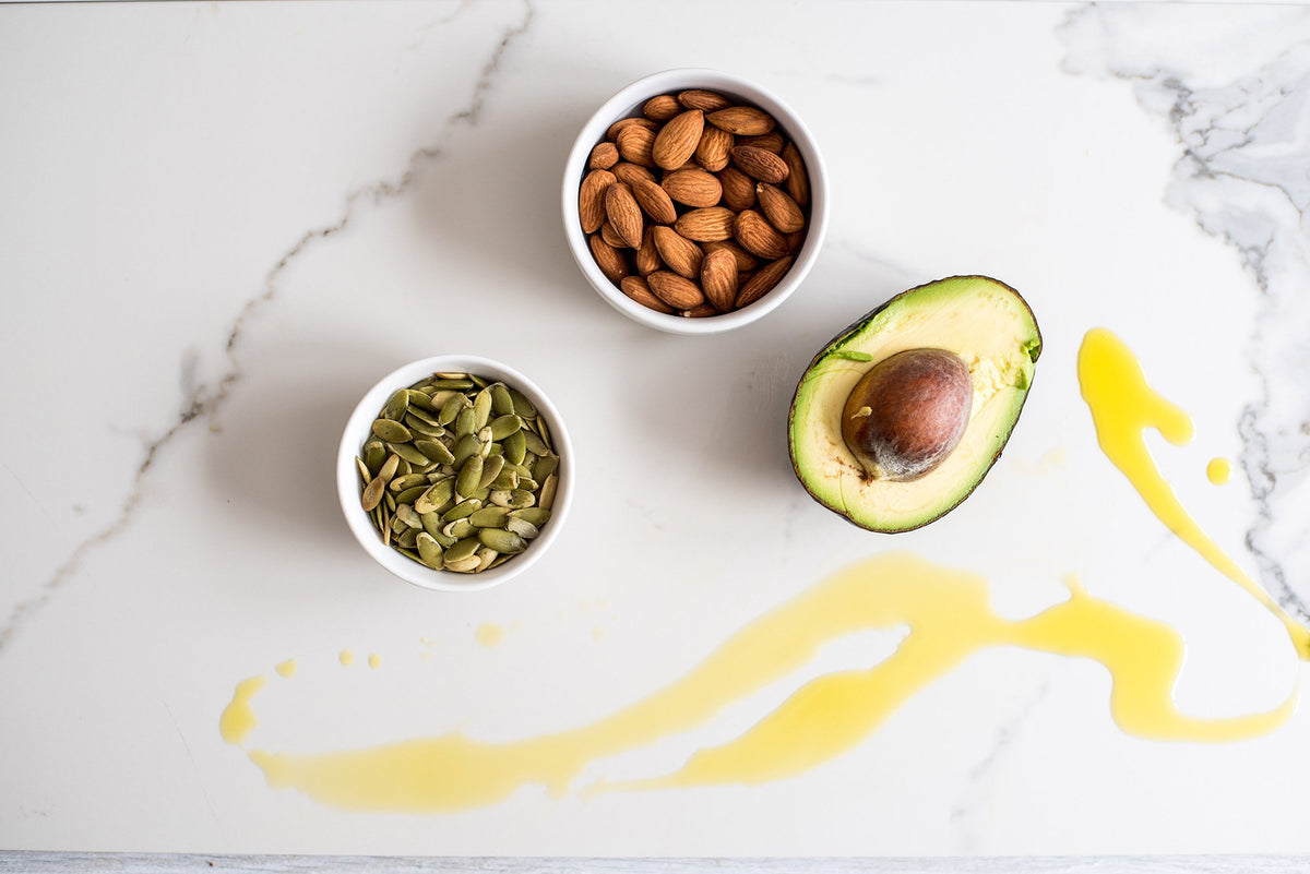 An avocado, almonds, sunflower seeds, coconut, and honey on a kitchen counter