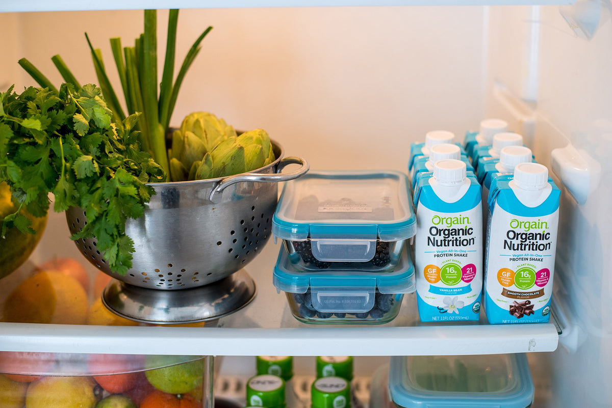 A fridge shelf with fresh greens, fruits, and Orgain protein shakes.