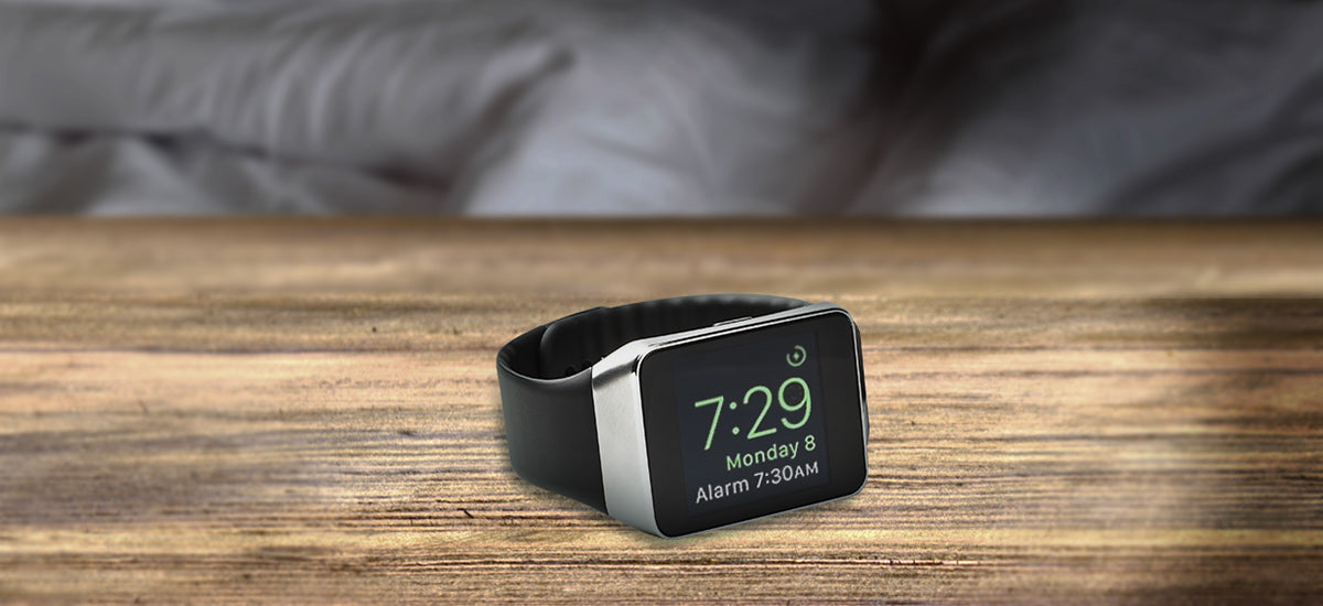 A digital smartwatch displaying the time 7:29 and an alarm set for 7:30 AM, resting on a wooden surface.