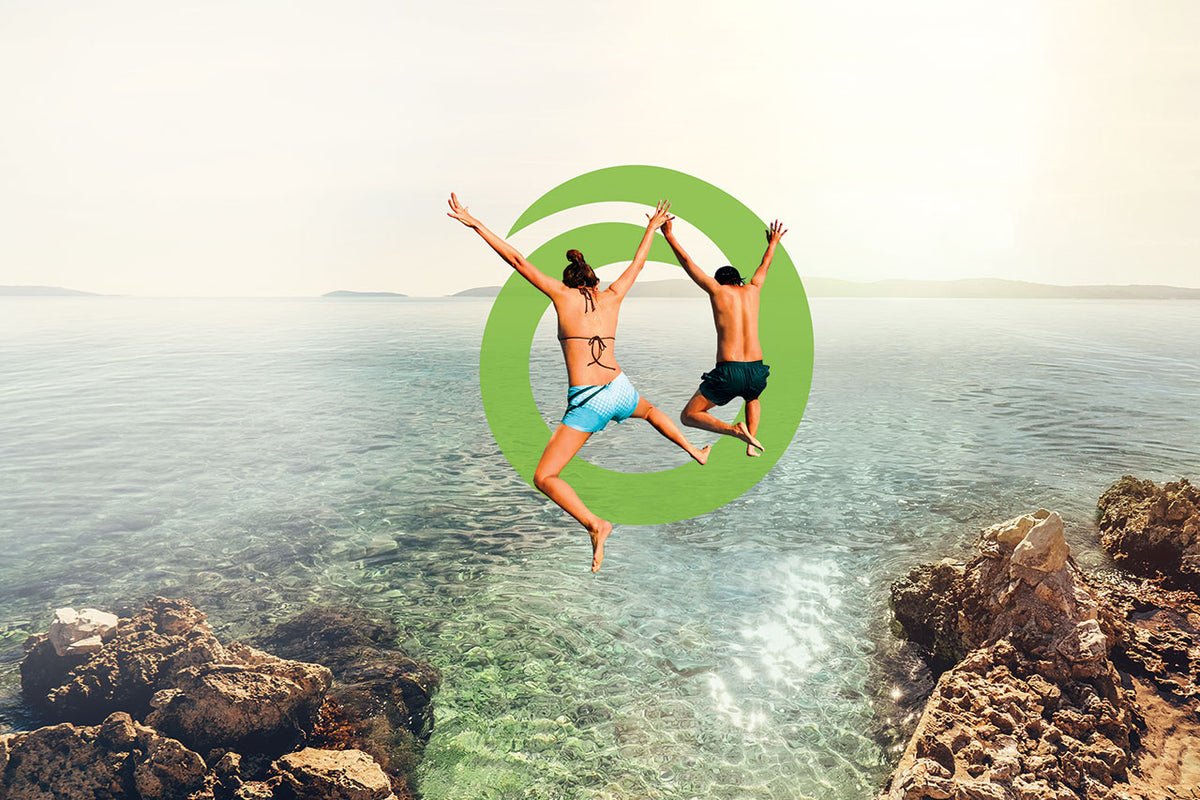 Two people jumping into the Orgain logo that is superimposed onto the sea
