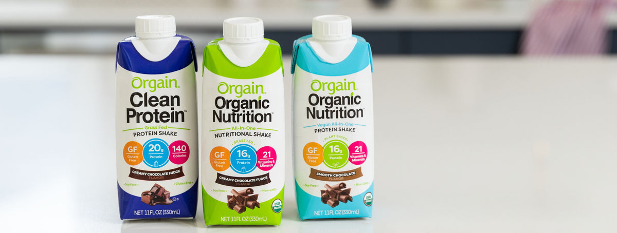 Three cartons of Orgain nutritional drinks, each labeled Creamy Chocolate Fudge, displayed side by side on a kitchen counter.