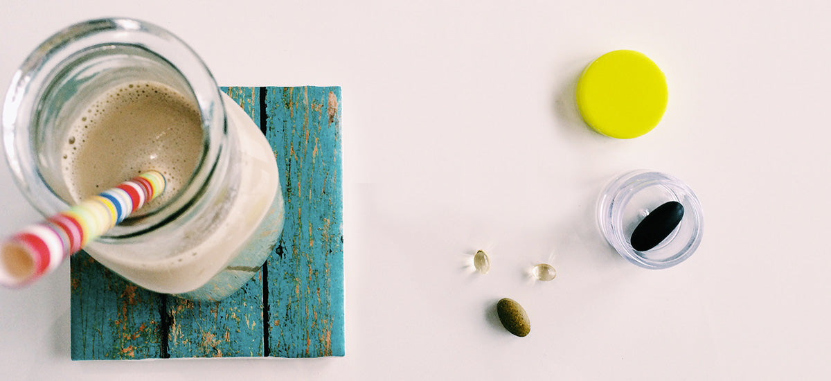Top view of a smoothie in a glass bottle with a colorful straw, supplements, and a container with a yellow lid.