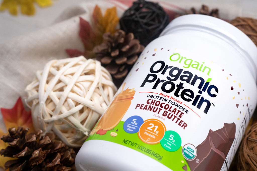 Orgain Organic Protein powder surrounded by autumnal decorations. Highlights 21g protein and 5g fiber per serving.