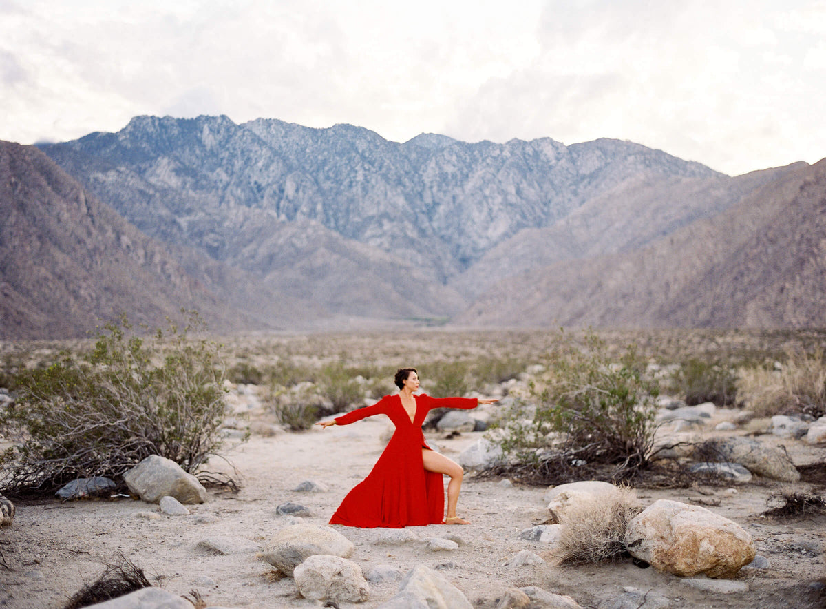 A woman in a red dress doing yoga in the desert mountatin valley.