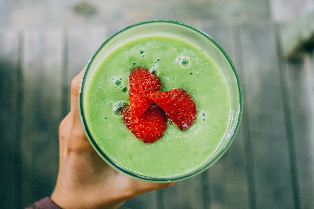 A woman's hand holding a green smoothie with sliced strawberries on top.