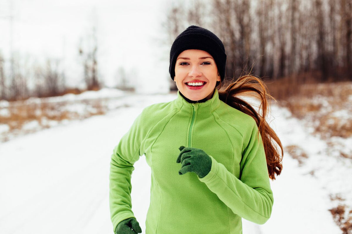 A happy female athlete running down a snow-covered road.