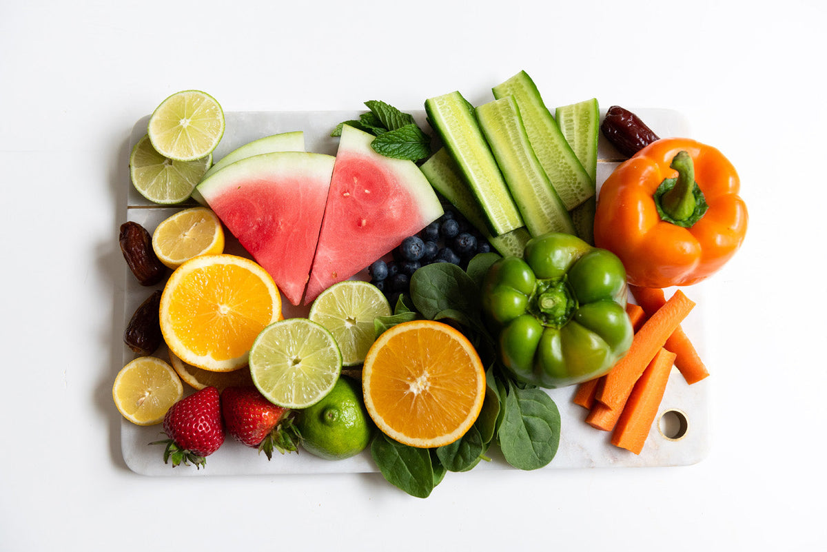 An assortment of fresh fruits and vegetables on a white surface, including cucumbers, citrus, watermelon, strawberries, and more.