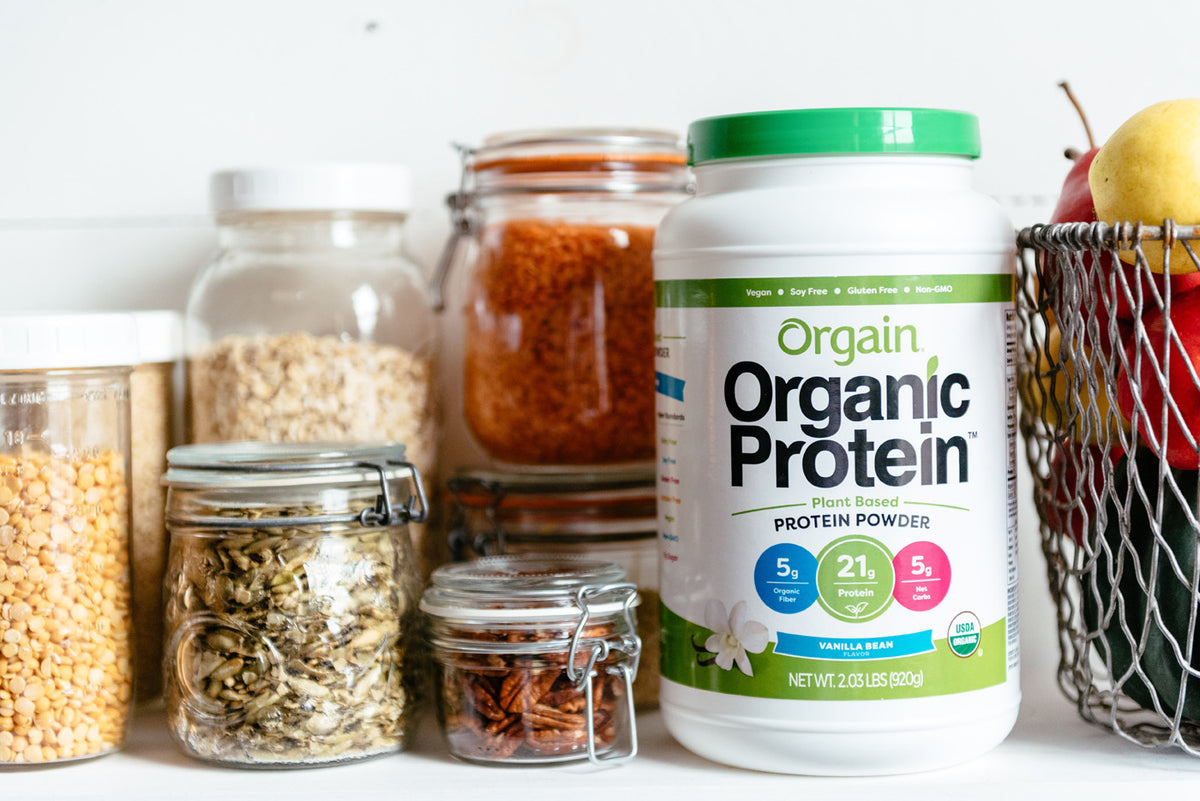 orgain organic protein plant based protein powder next to jars of nuts and grains