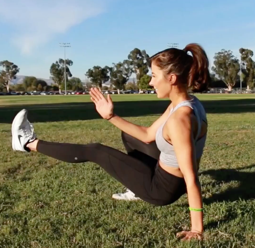 A woman exercising outside in the grass.