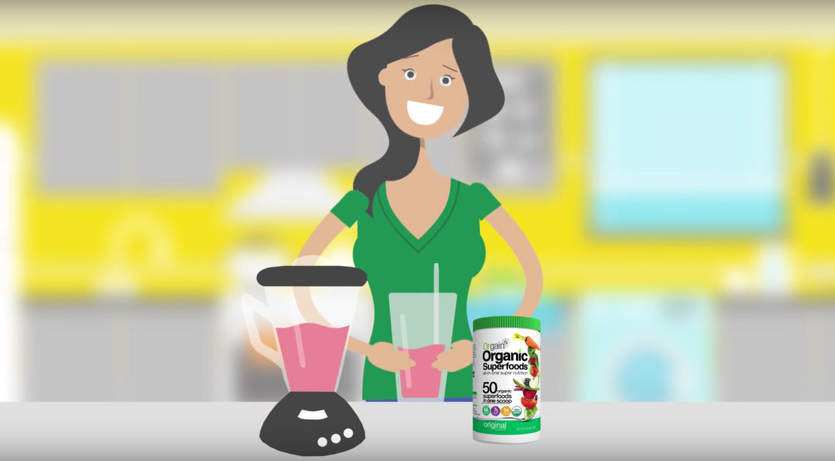 Illustration of a smiling woman in a green shirt standing in a kitchen. She is holding a glass of pink smoothie next to a blender containing the same liquid. A container of "Organic Superfoods" powder is on the counter beside her.