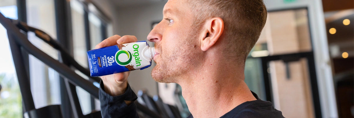 Man drinking from a blue and white container with a logo, indoors.